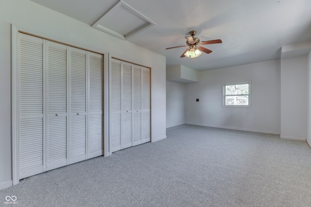 unfurnished bedroom with ceiling fan, light carpet, and multiple closets