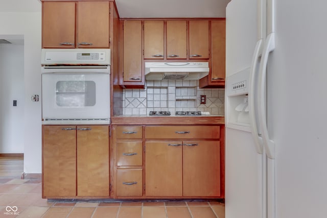 kitchen featuring white appliances, backsplash, light tile patterned floors, and tile countertops