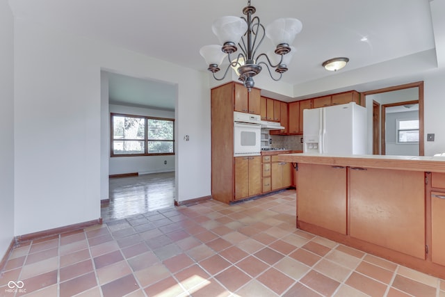 kitchen featuring white appliances, backsplash, pendant lighting, light tile patterned floors, and a chandelier