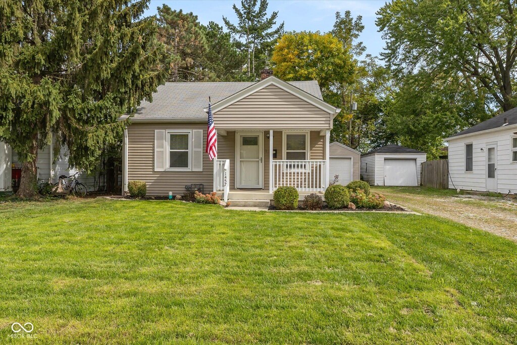 bungalow-style house featuring covered porch, a garage, a front lawn, and an outdoor structure