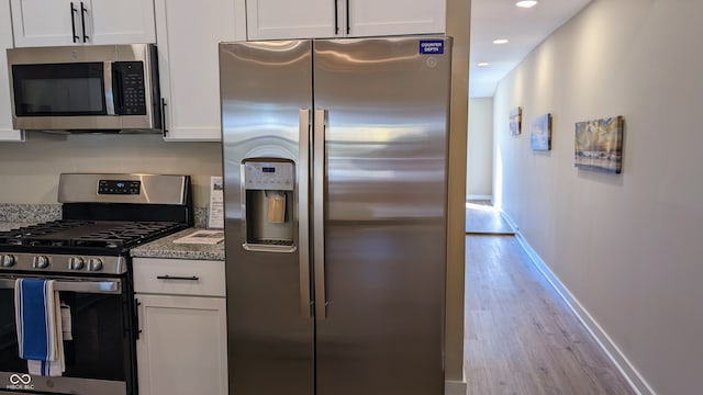 kitchen with stainless steel appliances, light stone countertops, white cabinets, and light wood-type flooring