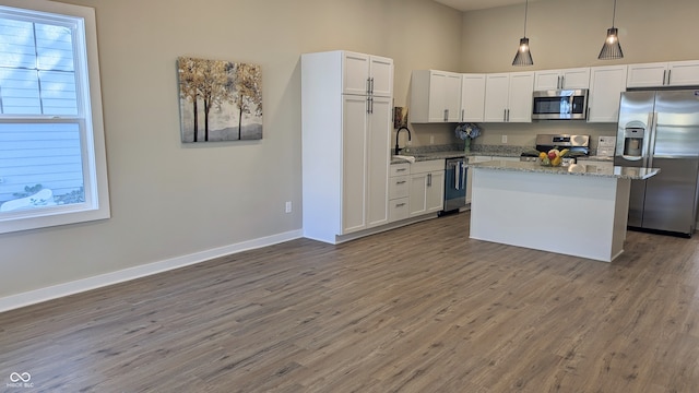 kitchen with a kitchen island, appliances with stainless steel finishes, decorative light fixtures, white cabinetry, and light stone countertops