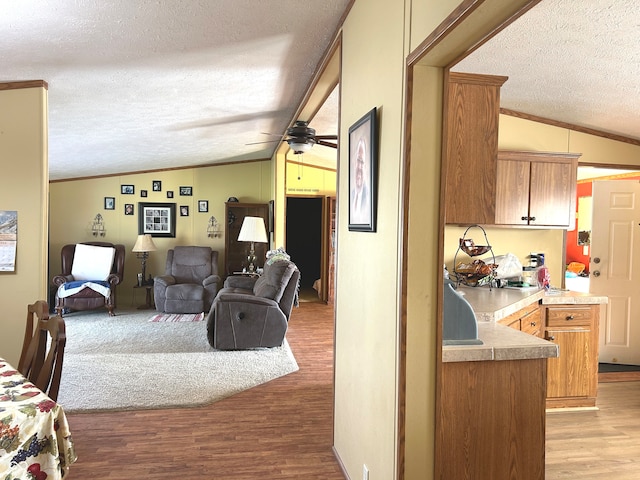 living room with vaulted ceiling, ceiling fan, ornamental molding, light wood-type flooring, and a textured ceiling