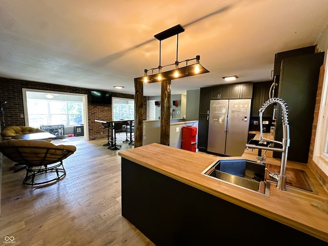 kitchen with stainless steel refrigerator, light hardwood / wood-style flooring, butcher block counters, sink, and brick wall