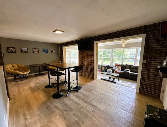 dining space featuring light hardwood / wood-style floors, brick wall, and ceiling fan