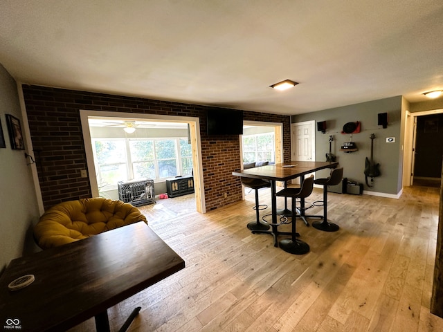 dining area with light hardwood / wood-style floors, brick wall, and ceiling fan