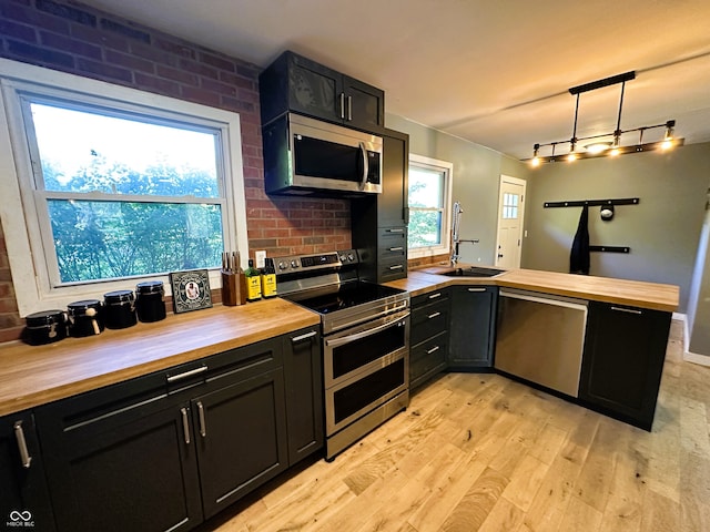 kitchen featuring brick wall, appliances with stainless steel finishes, light hardwood / wood-style floors, and butcher block counters