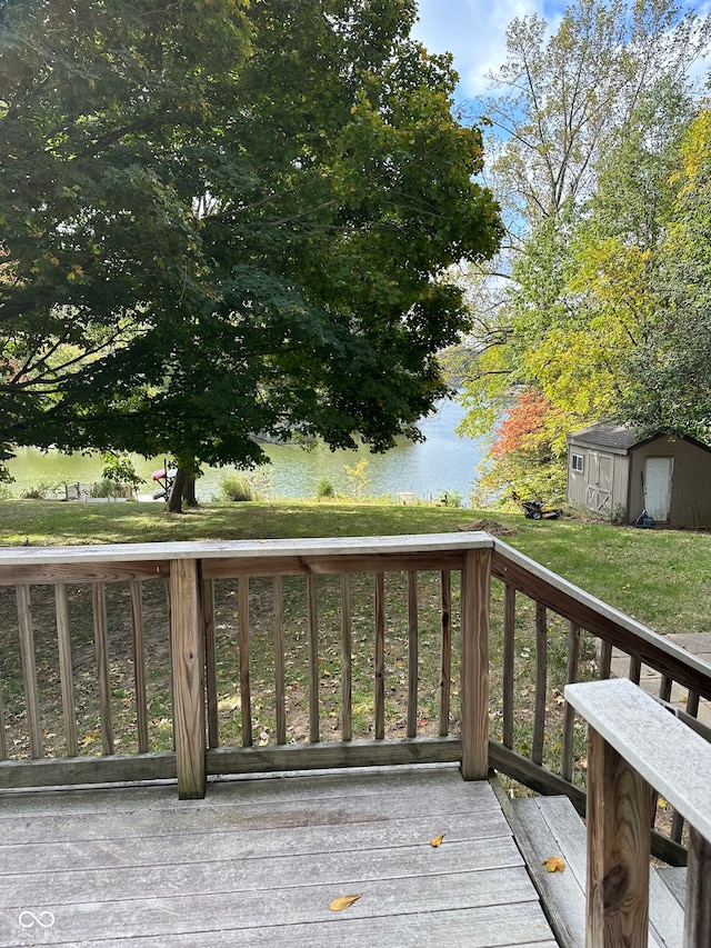 wooden terrace with a water view, a storage unit, and a yard