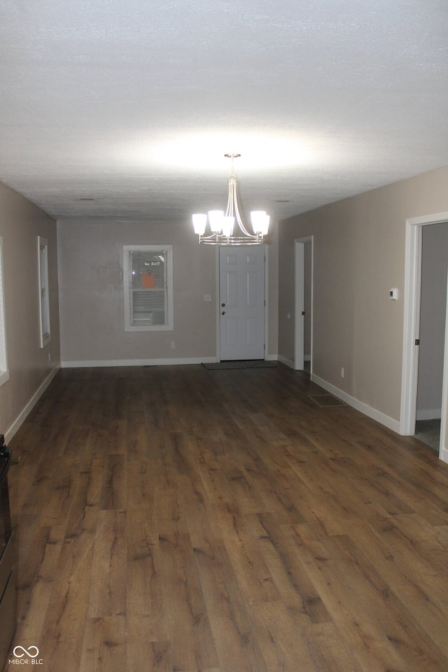 empty room with dark hardwood / wood-style flooring, a notable chandelier, and a textured ceiling