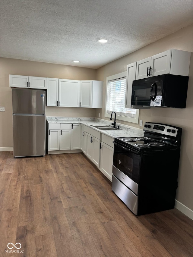 kitchen with stainless steel appliances, white cabinetry, a textured ceiling, sink, and hardwood / wood-style floors