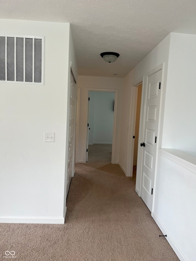 corridor featuring a textured ceiling and light colored carpet