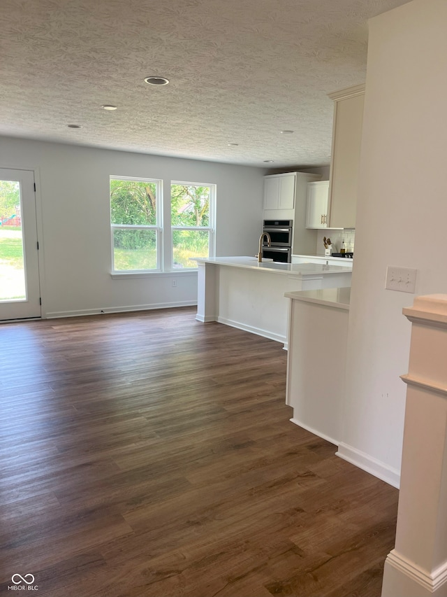 kitchen featuring white cabinets, a textured ceiling, dark wood-type flooring, double oven, and a breakfast bar