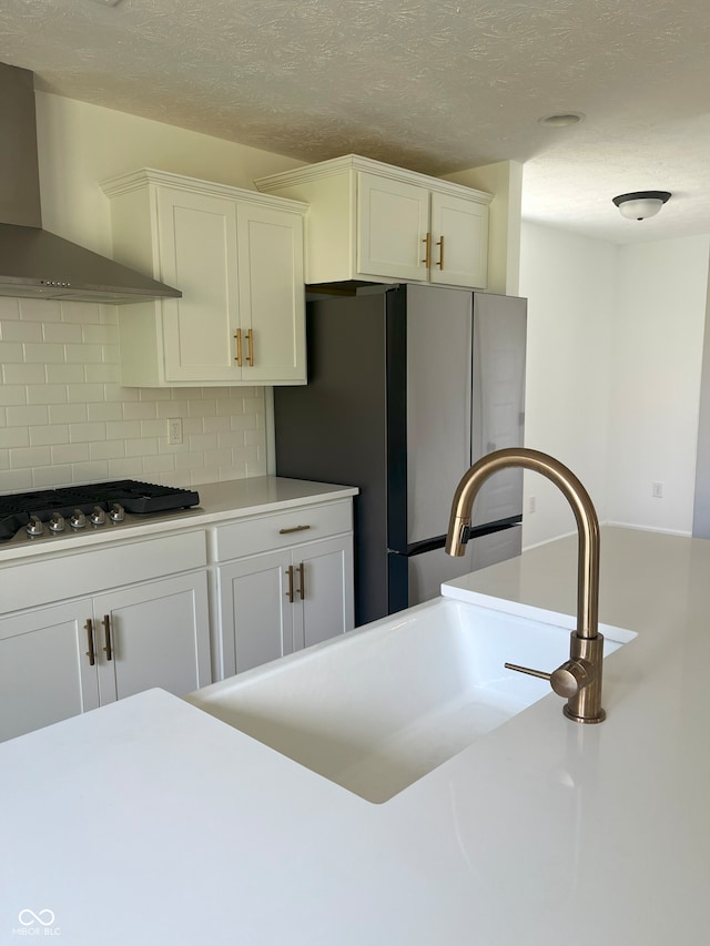 kitchen with decorative backsplash, white cabinets, gas cooktop, sink, and wall chimney range hood