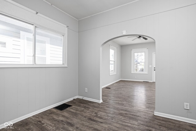 empty room with ceiling fan, wood walls, and dark wood-type flooring