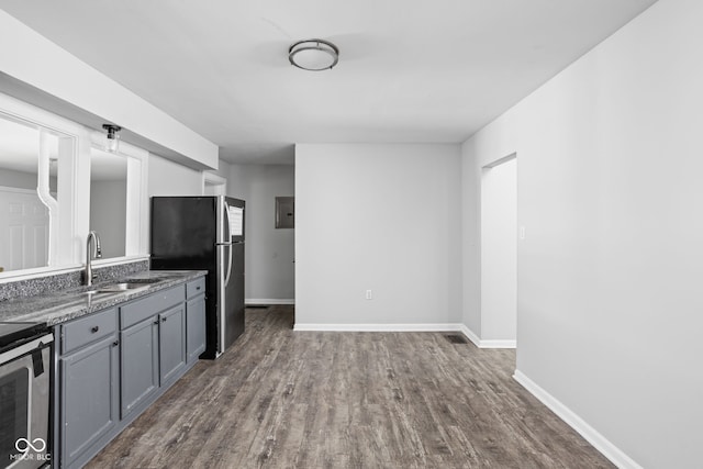 kitchen with sink, dark wood-type flooring, gray cabinets, stainless steel appliances, and dark stone counters