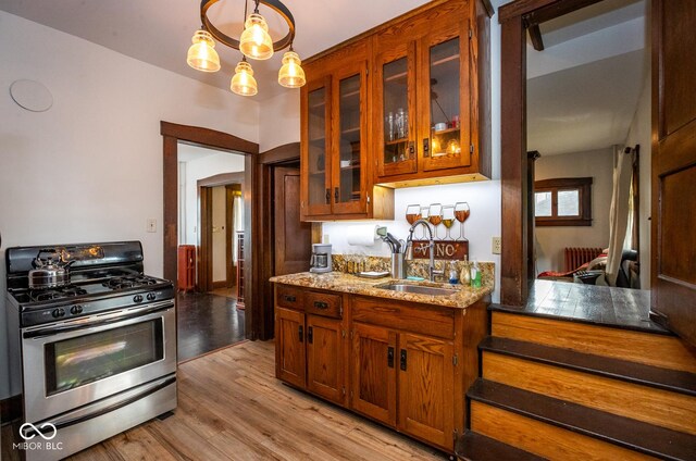 1457 Fairfield Ave, Indianapolis, IN 46205 - kitchen featuring light stone counters, stainless steel gas range oven, a sink, light wood-style floors, and glass insert cabinets