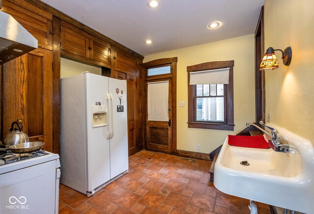 1457 Fairfield Ave, Indianapolis, IN 46205 - kitchen featuring a sink, baseboards, white appliances, stone finish flooring, and wall chimney range hood