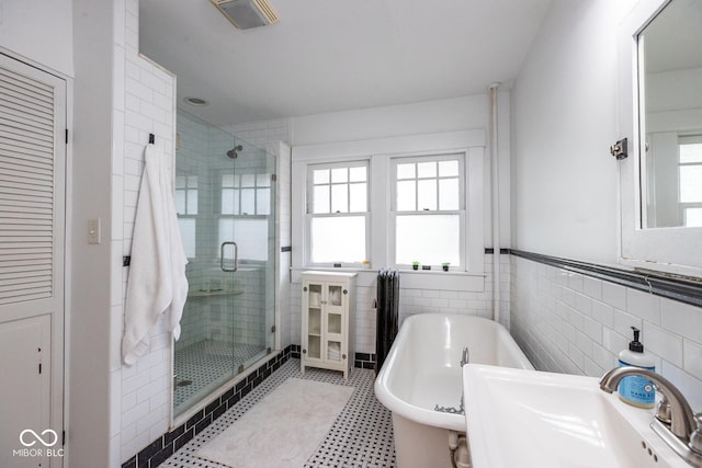 full bath with a sink, a stall shower, a freestanding tub, tile walls, and a wainscoted wall