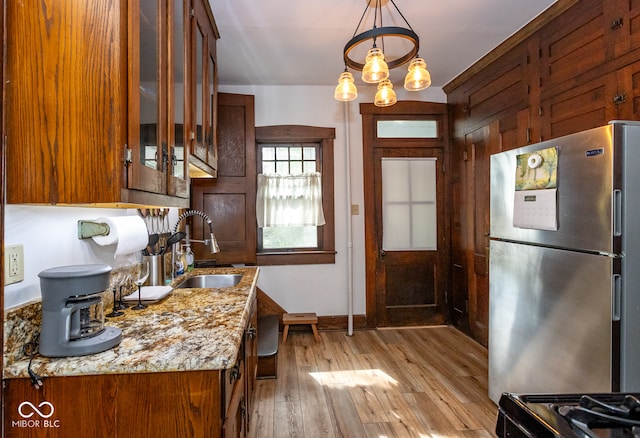 kitchen with light hardwood / wood-style flooring, hanging light fixtures, sink, light stone countertops, and stainless steel refrigerator