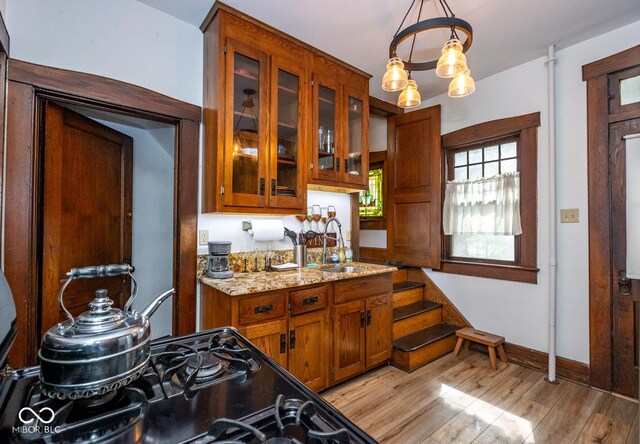 kitchen featuring brown cabinetry, glass insert cabinets, light wood-type flooring, and a sink