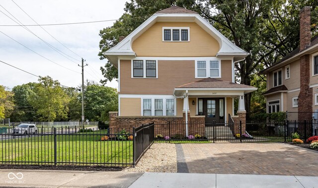 traditional style home featuring a porch, brick siding, a front yard, and a fenced front yard