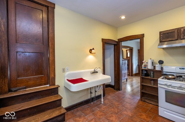 interior space with white gas range oven, baseboards, dark brown cabinetry, recessed lighting, and under cabinet range hood
