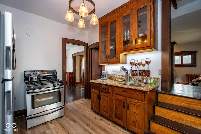 kitchen featuring light wood finished floors, light stone counters, stainless steel appliances, a sink, and brown cabinetry
