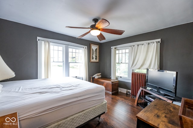 bedroom featuring dark wood-type flooring, ceiling fan, multiple windows, and radiator heating unit