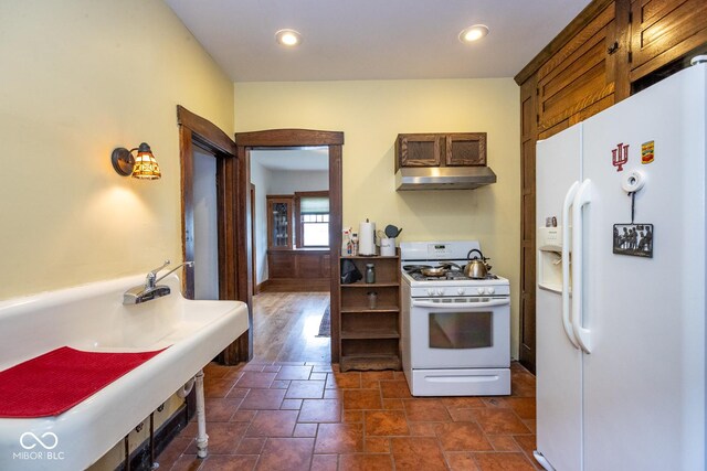 kitchen with a sink, white appliances, under cabinet range hood, stone finish floor, and recessed lighting
