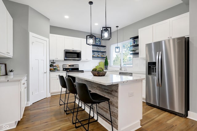 kitchen with white cabinets, a kitchen island, stainless steel appliances, light stone countertops, and dark hardwood / wood-style flooring