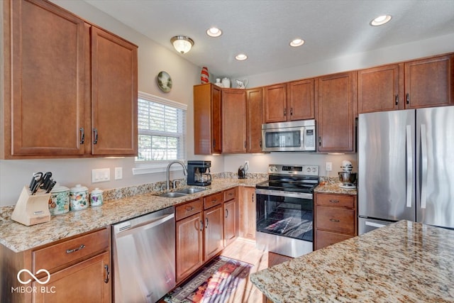 kitchen with light stone countertops, light hardwood / wood-style floors, appliances with stainless steel finishes, and sink