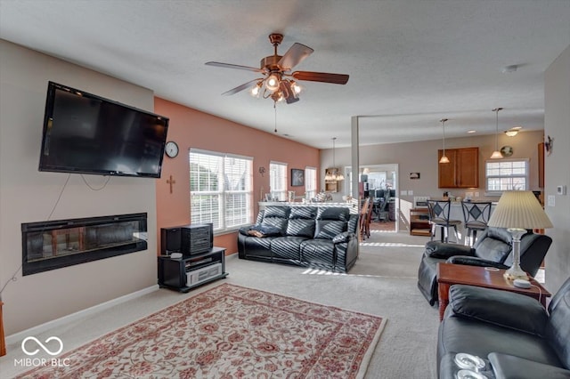 living room with light carpet, a textured ceiling, ceiling fan with notable chandelier, and a healthy amount of sunlight