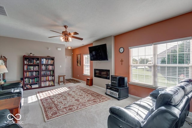 living room with ceiling fan, light colored carpet, a fireplace, and a textured ceiling