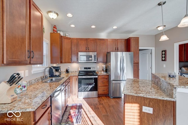 kitchen with light stone counters, sink, decorative light fixtures, appliances with stainless steel finishes, and hardwood / wood-style floors