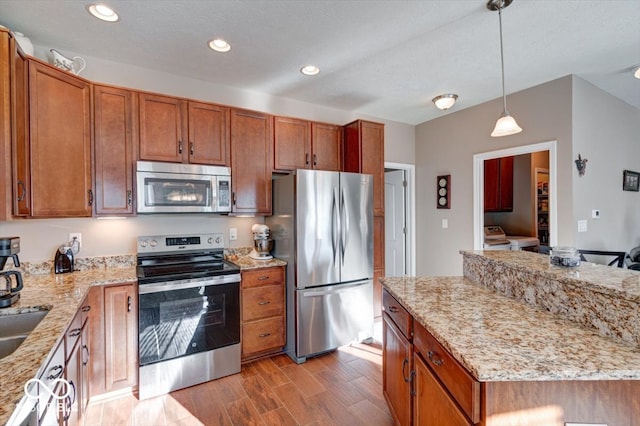 kitchen featuring light stone counters, pendant lighting, stainless steel appliances, and hardwood / wood-style flooring