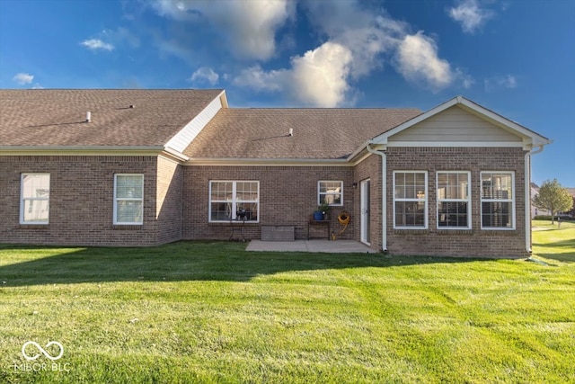 rear view of property with a yard, brick siding, a shingled roof, and a patio area