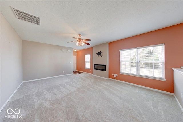 unfurnished living room with visible vents, ceiling fan, baseboards, carpet flooring, and a glass covered fireplace