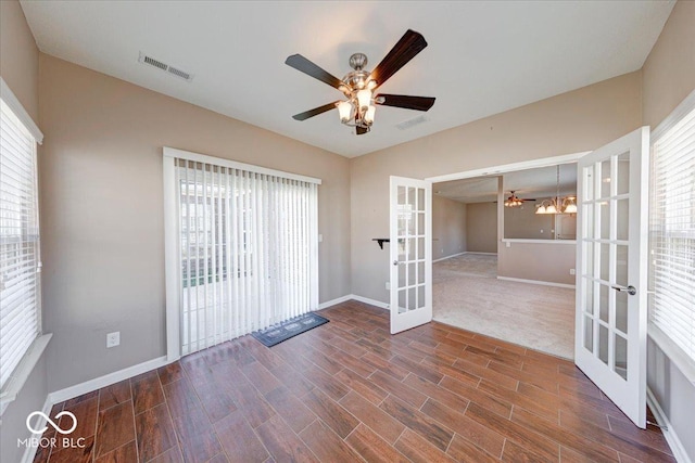 empty room with ceiling fan with notable chandelier, wood finished floors, french doors, and visible vents