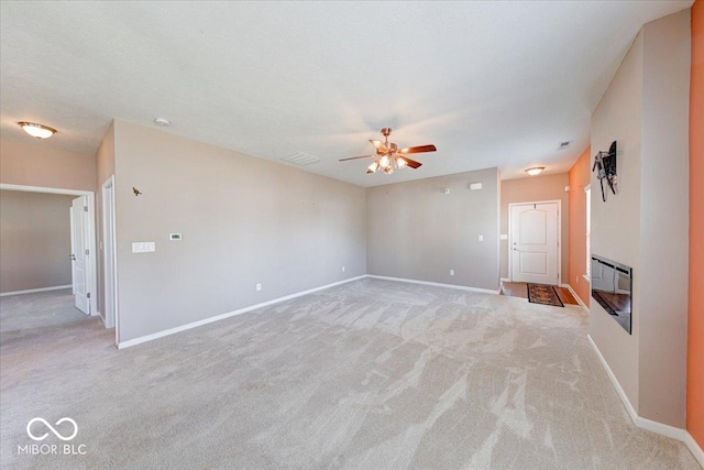 unfurnished living room featuring a glass covered fireplace, baseboards, and light carpet