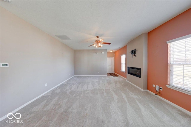 unfurnished living room featuring baseboards, visible vents, a textured ceiling, a glass covered fireplace, and light carpet