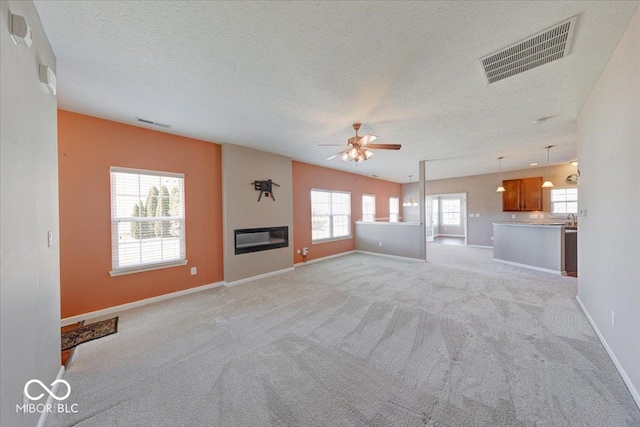 unfurnished living room with a glass covered fireplace, light colored carpet, visible vents, and baseboards