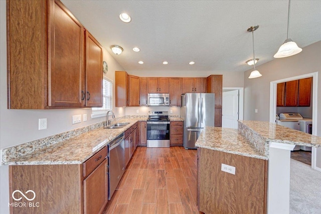 kitchen with light wood-type flooring, brown cabinets, independent washer and dryer, stainless steel appliances, and a sink