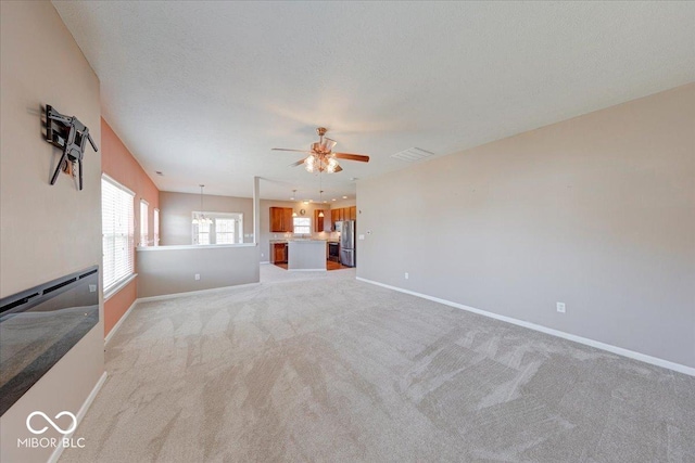 unfurnished living room featuring a textured ceiling, baseboards, light colored carpet, and ceiling fan with notable chandelier