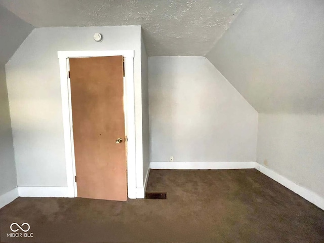 additional living space featuring lofted ceiling, dark colored carpet, and a textured ceiling