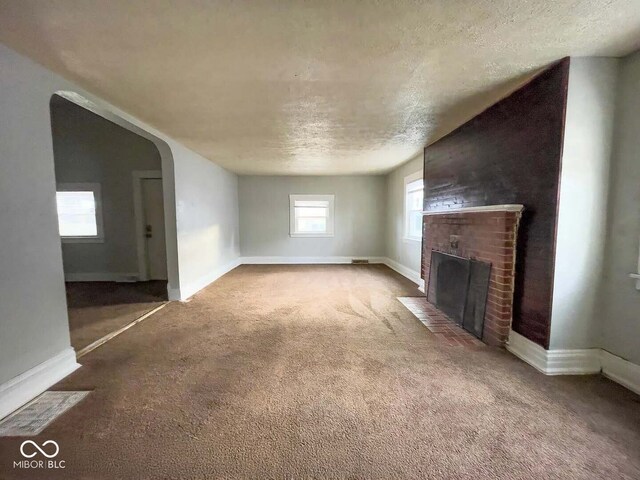 unfurnished living room with a brick fireplace, carpet floors, and a textured ceiling