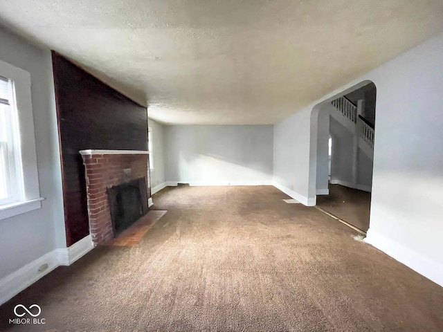 unfurnished living room with a brick fireplace and dark colored carpet