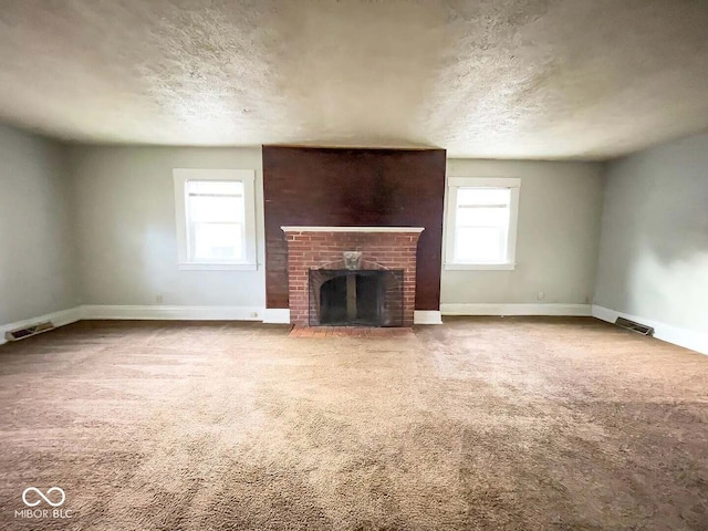 unfurnished living room featuring a brick fireplace, a textured ceiling, plenty of natural light, and carpet flooring