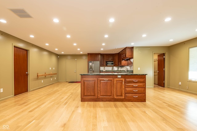 kitchen featuring light hardwood / wood-style flooring, stainless steel appliances, dark stone countertops, and a center island with sink