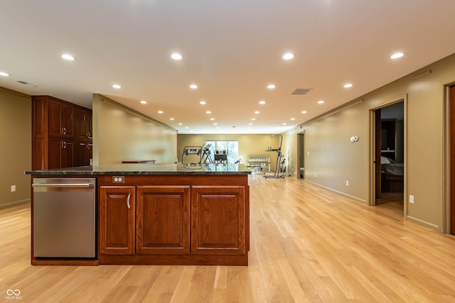 kitchen with ornamental molding, stainless steel dishwasher, a kitchen island with sink, light hardwood / wood-style flooring, and dark stone counters