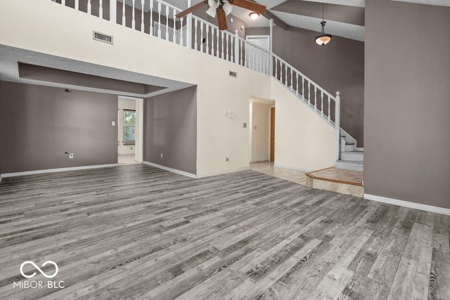 unfurnished living room with a towering ceiling, wood-type flooring, and ceiling fan